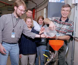 Ken Stanfield (right) pours the ceremonial final cupful oil into the MiniBooNE detector, assisted by Eric Hawker. Looking on are Jennifer Raaf and co-spokespersons Bill Louis and Janet Conrad.