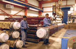 Doug Kelley (left) and Cliff Besch remove a spare Tevatron dipole magnet by overhead crane, in the Magnet Storage Building. Material Control keeps track of more than 1,000 backup magnets.