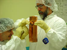 Project manager Dan Bauer from Fermilab holds one tower of detectors as Vuk Mandic from UC Berkeley examines them. Each tower of detectors contains 1 kilogram of germanium for detecting dark matter and 200 grams of silicon to distinguish WIMPs from neutrons. Thin layers of silicon, aluminum, and tungsten covering the detector surfaces measure both the heat and charge released when a particle interacts inside. 